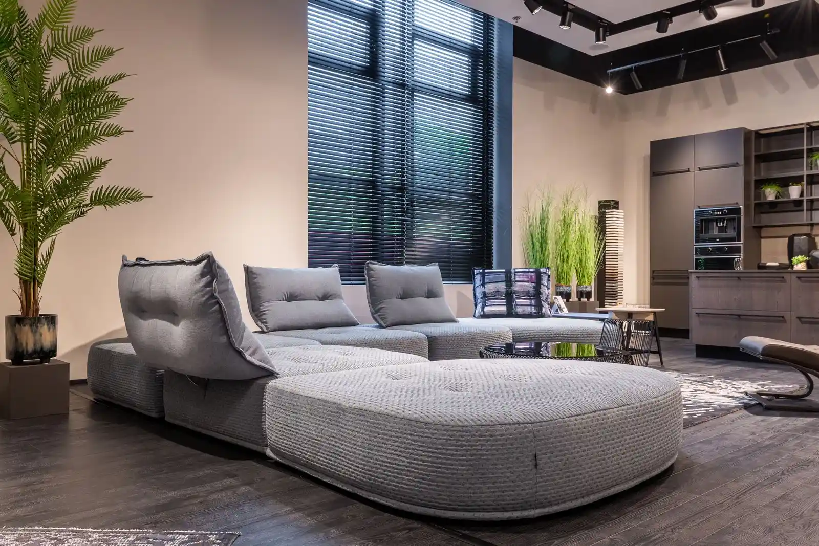 Modern living room with a large grey sofa, plants and an open kitchen
