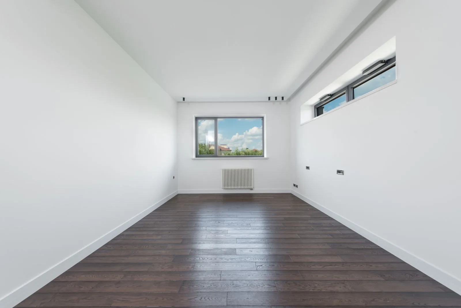 Empty, unfurnished apartment room with dark wooden floor and white walls